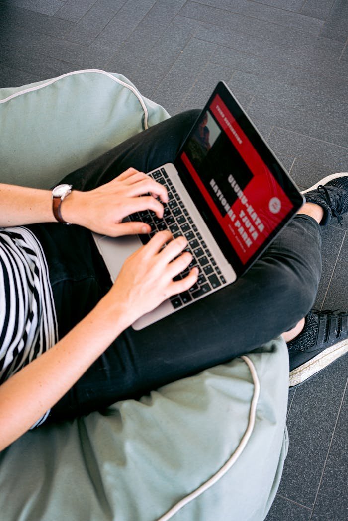 Services Person working remotely on a laptop while sitting comfortably on a beanbag chair indoors.
